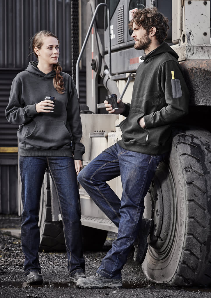 Two individuals wearing black hoodies and blue stretch denim work jeans, standing by a large vehicle.