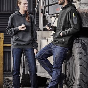A pair of people wearing black hoodies and blue stretch denim work jeans, standing beside a large vehicle tire.