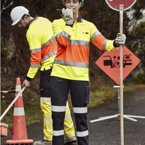 A woman in high-visibility workwear holds a stop sign, while a man in similar gear works nearby. Both wear hard hats.