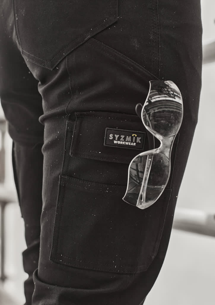 A close-up of black cargo pants with a logo and clear sunglasses tucked into the pocket.