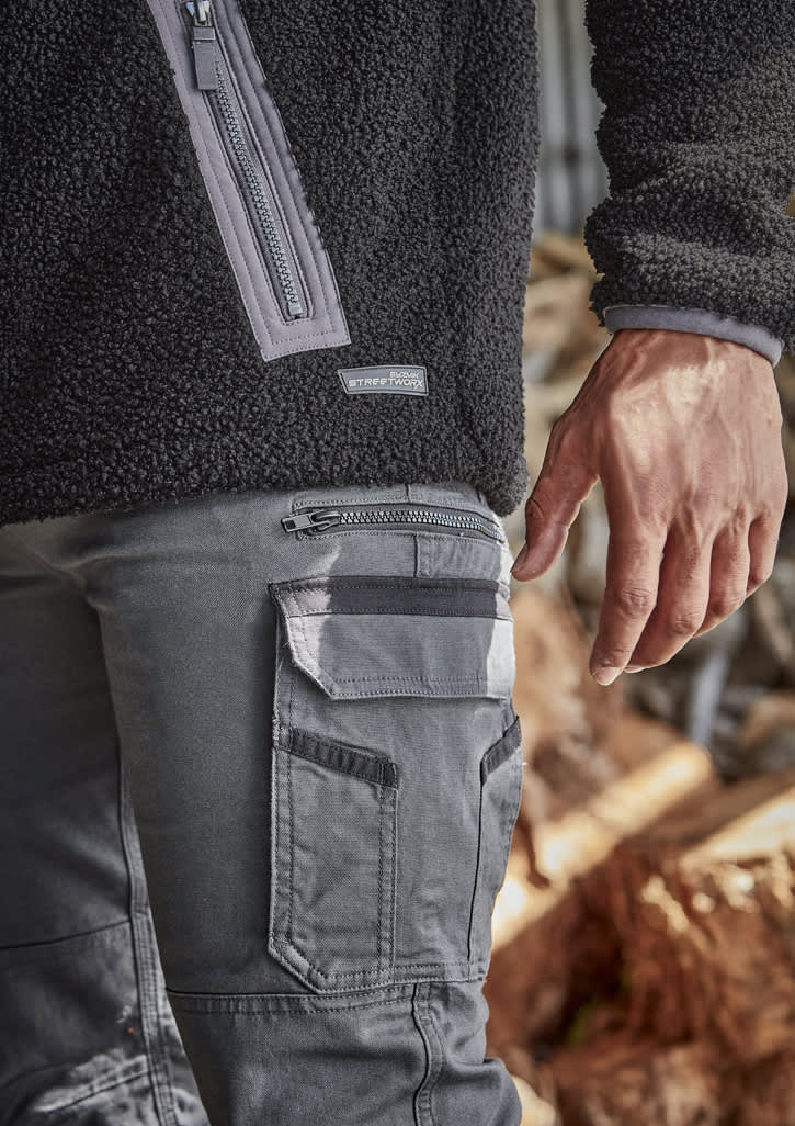 A close-up of men's grey work pants featuring multiple pockets and a zipped side pocket, paired with a black fleece top.