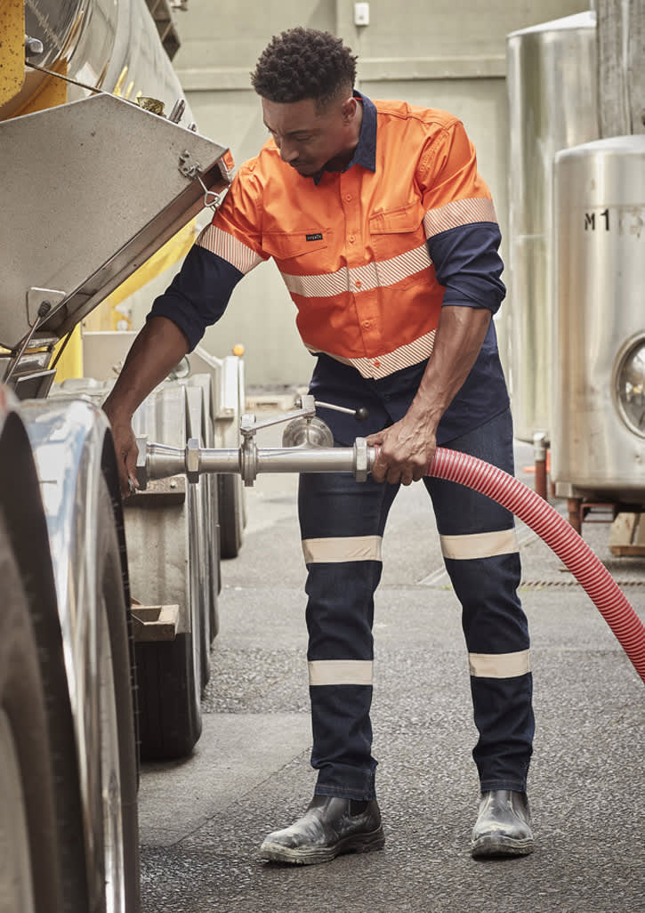 A worker in orange and navy bio motion taped stretch jeans operates equipment in a work environment, featuring reflective strips.