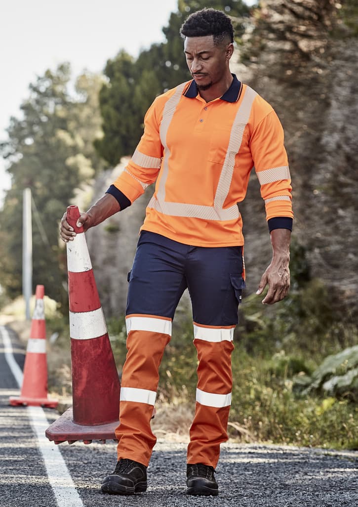 Hi-vis orange and navy work pants with reflective tape, worn by a man holding a traffic cone on a rural road.