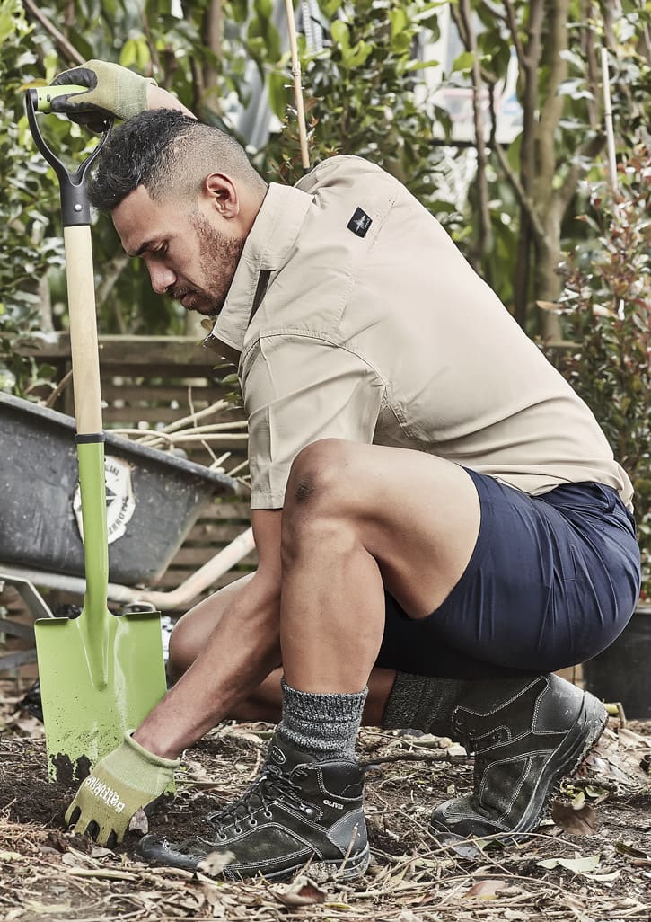 Men's lightweight outdoor shorts in navy, paired with a beige shirt, worn by a man kneeling with a shovel in a garden.