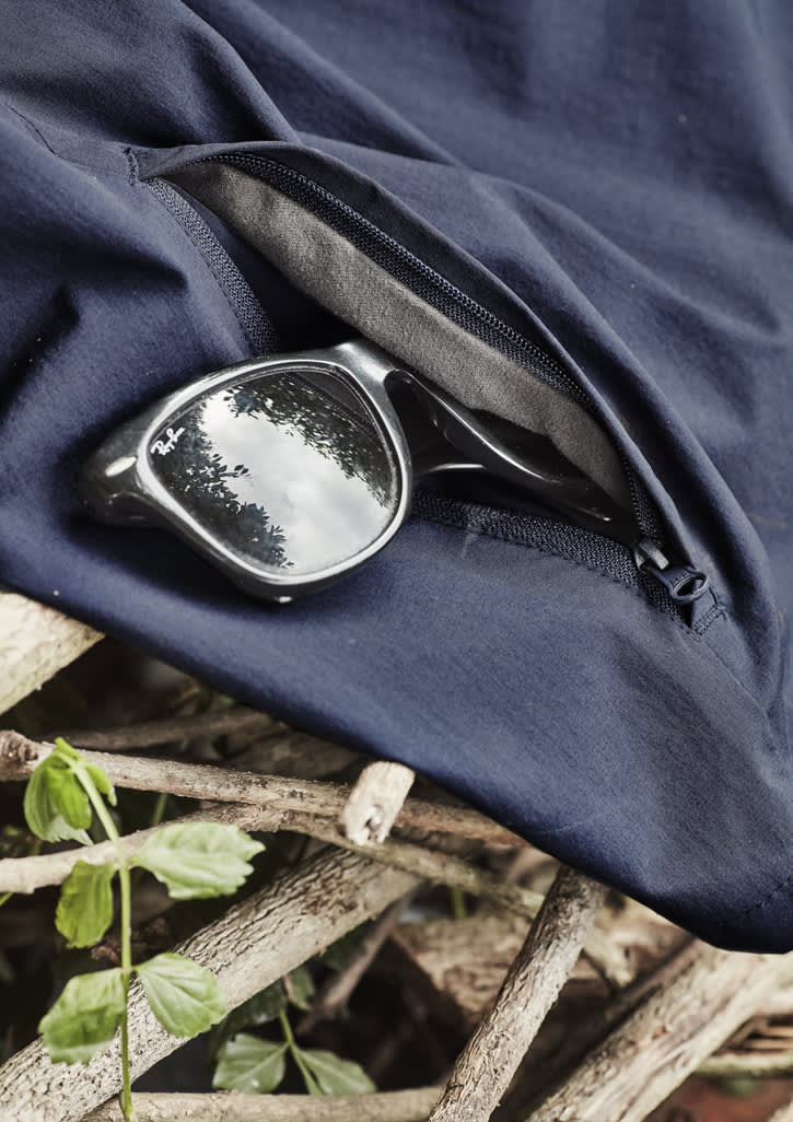 A pair of black sunglasses rests on navy lightweight shorts with a zippered pocket, placed on a textured surface.