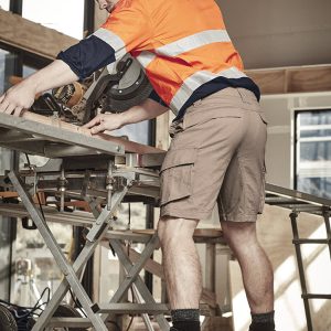 Curved cargo shorts in a light tan colour, worn by a man working on a construction site with ear protection.