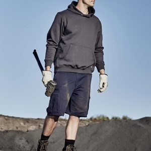 A man in a grey hoodie and navy cargo shorts stands outdoors, wearing a hard hat and gloves, holding a tool.
