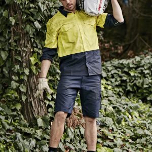 Men's rugged cooling vented shorts in navy, styled with a bright yellow shirt, set against a leafy background.