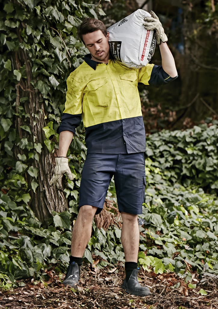 Men's rugged cooling vented shorts in navy, styled with a bright yellow shirt, set against a leafy background.