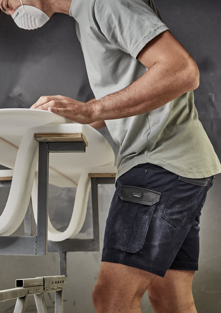 A man wearing navy rugged cooling stretch shorts and a grey t-shirt, working at a table with a surfboard.