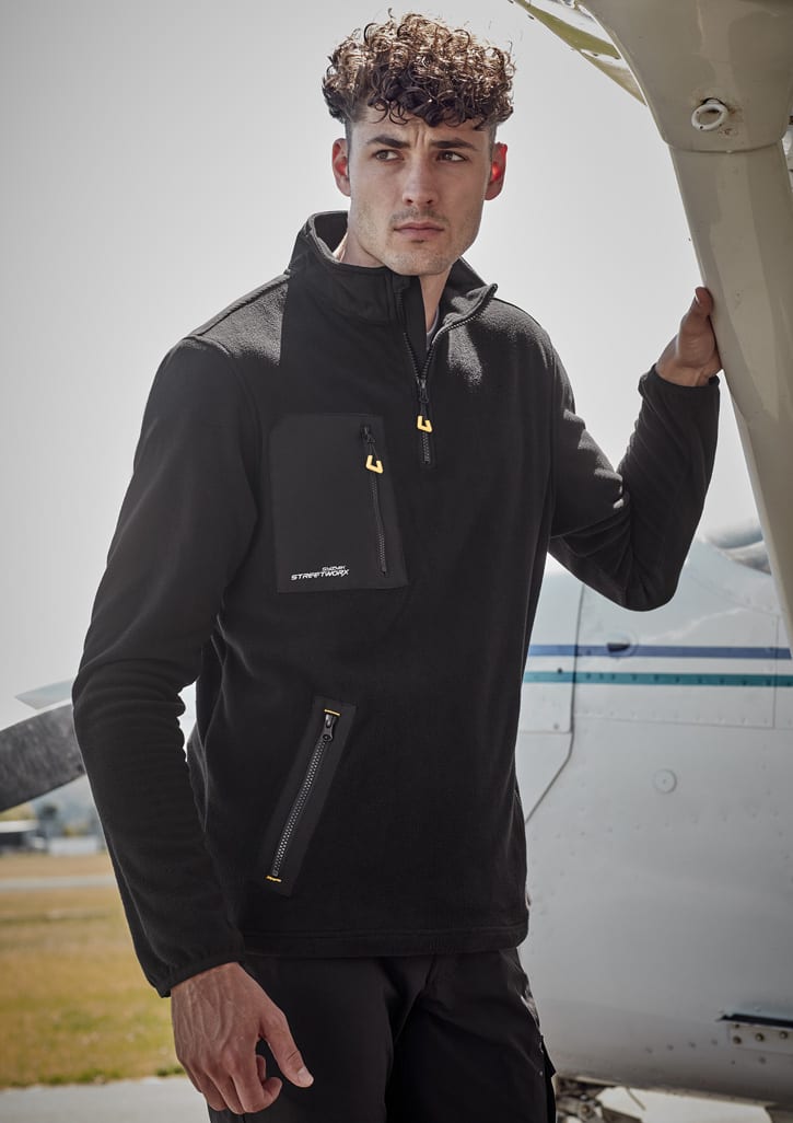 A model wearing a black unisex lightweight 1/4 zip polar fleece with a front pocket, standing next to an aircraft.