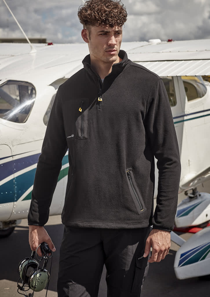 A black lightweight 1/4 zip polar fleece is worn by a model near a small aircraft, featuring a zip pocket and branding.