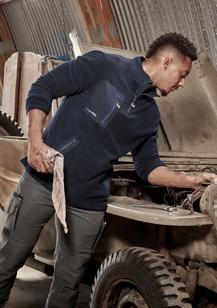 A man in a navy lightweight 1/4 zip polar fleece, working on a vehicle, with a logo on the garment.