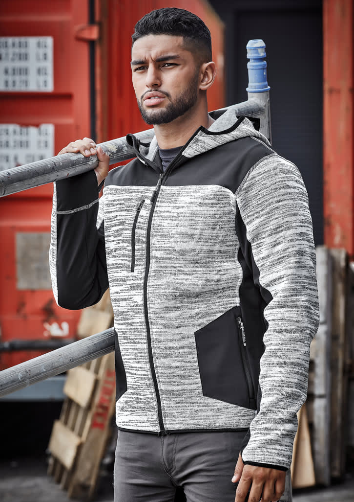 A man wearing a black and grey striped unisex reinforced knit hoodie, holding a metal ladder against a red backdrop.