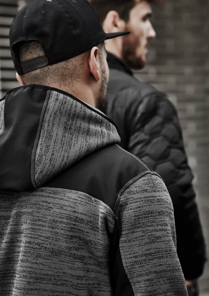A unisex reinforced knit hoodie in grey with a black hood, featuring a logo on the back, worn by a person.