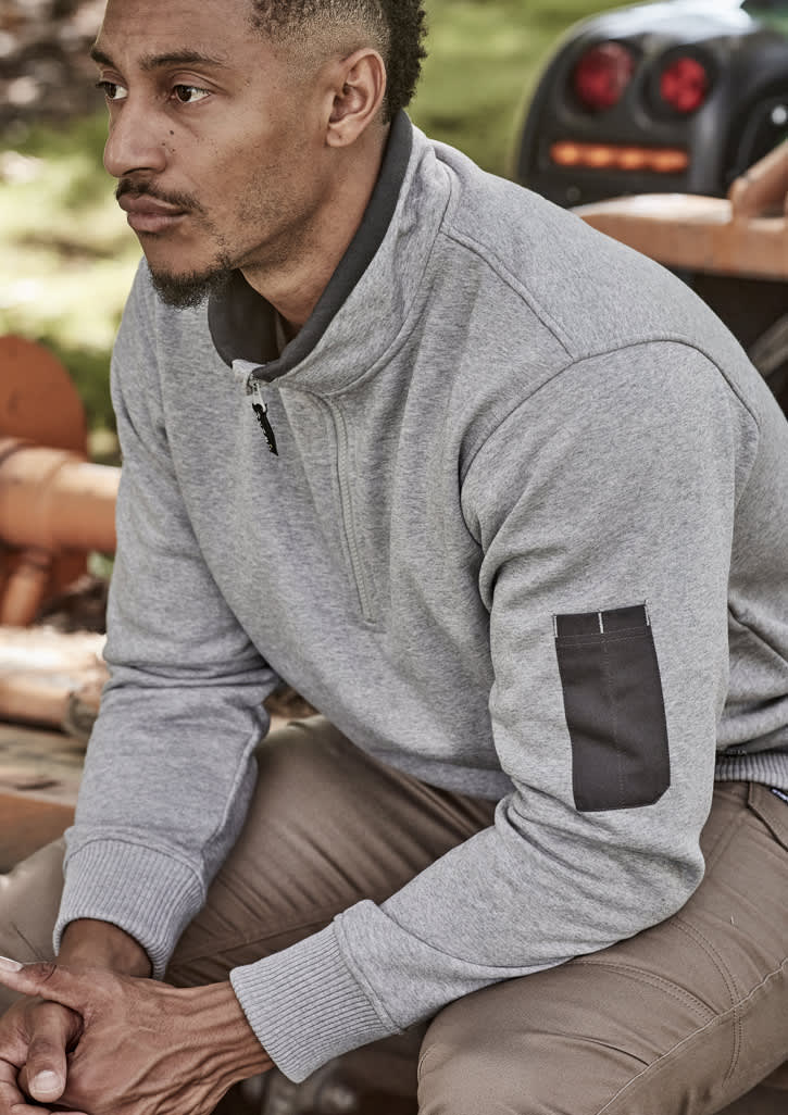 A man wearing a grey unisex 1/4 zip brushed fleece pullover with a logo on the sleeve, seated outdoors.