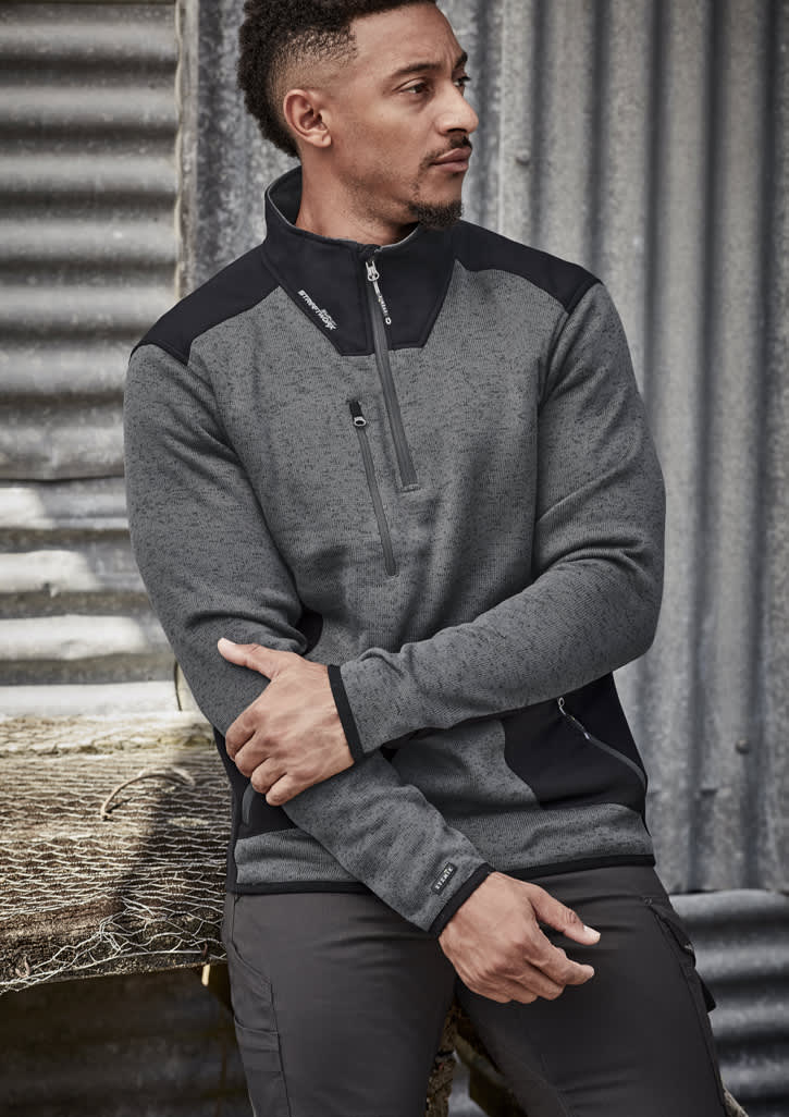 A grey and black unisex pullover with a 1/2 zip and a logo, set against a textured background.