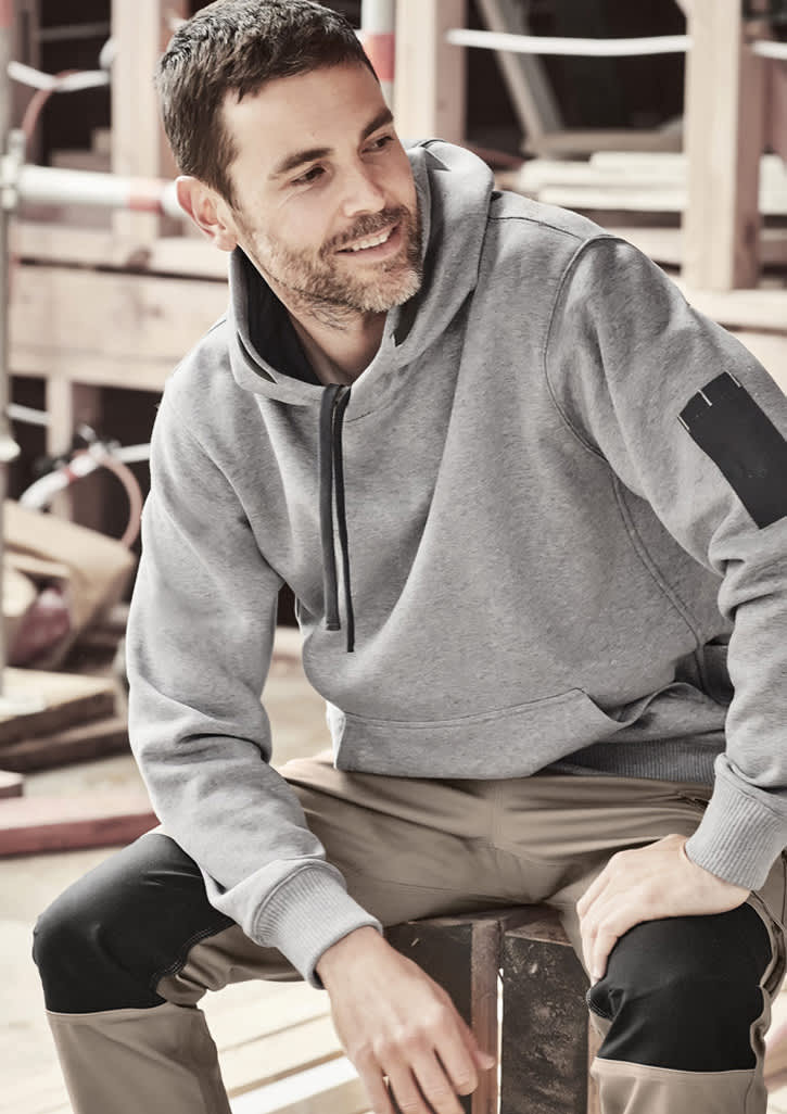 A grey unisex multi-pocket hoodie featuring a logo, worn by a person sitting on a wooden surface.