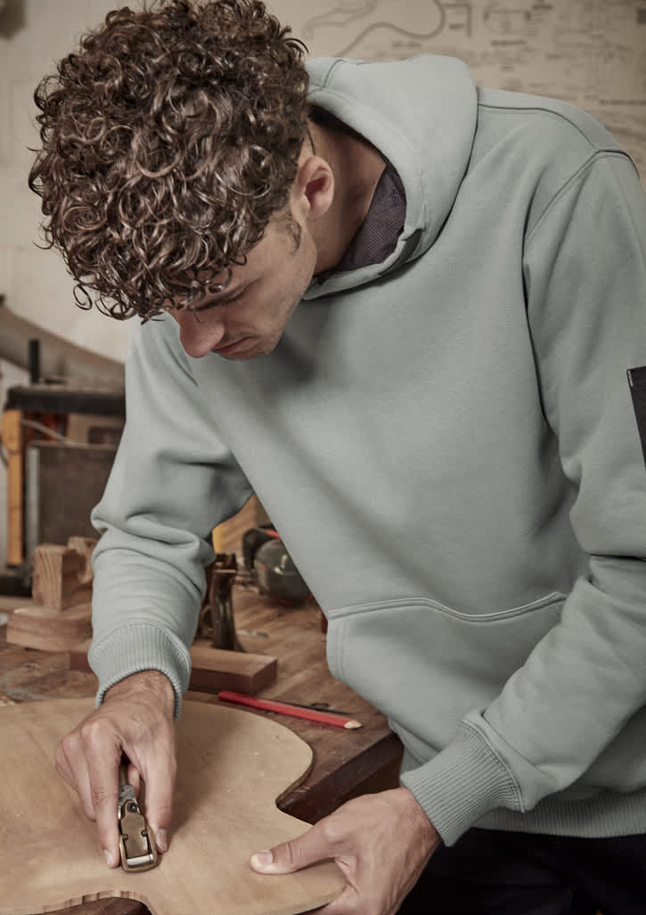 A unisex multi-pocket hoodie in green worn by a person working on wood, featuring a logo on the sleeve.