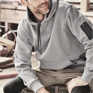 A grey unisex multi-pocket hoodie is worn by a man seated on a wooden bench, with worksite equipment in the background.