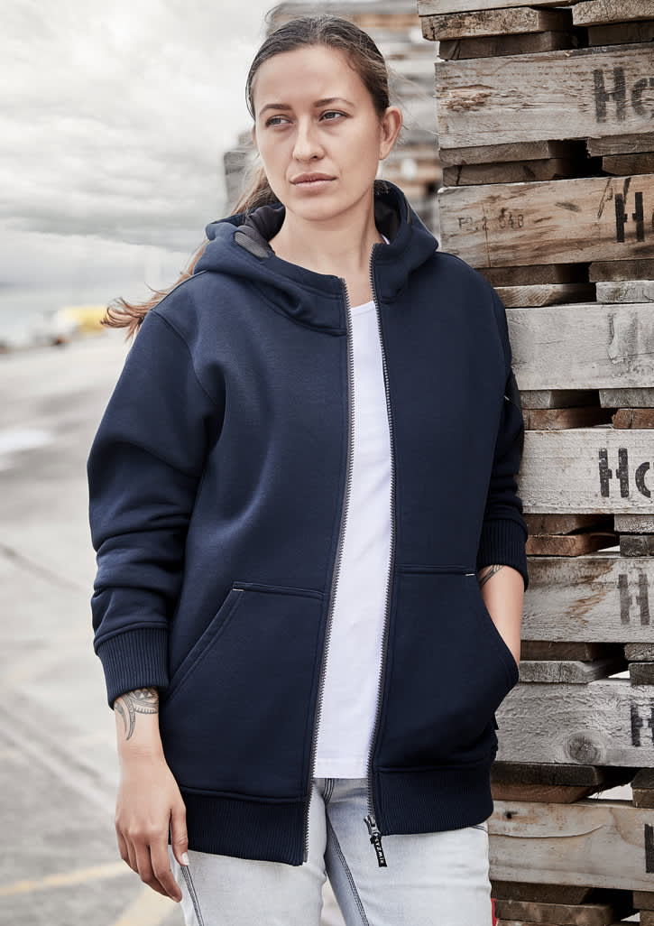 A navy unisex zip front hoodie with multiple pockets, worn by a woman against a backdrop of wooden pallets.