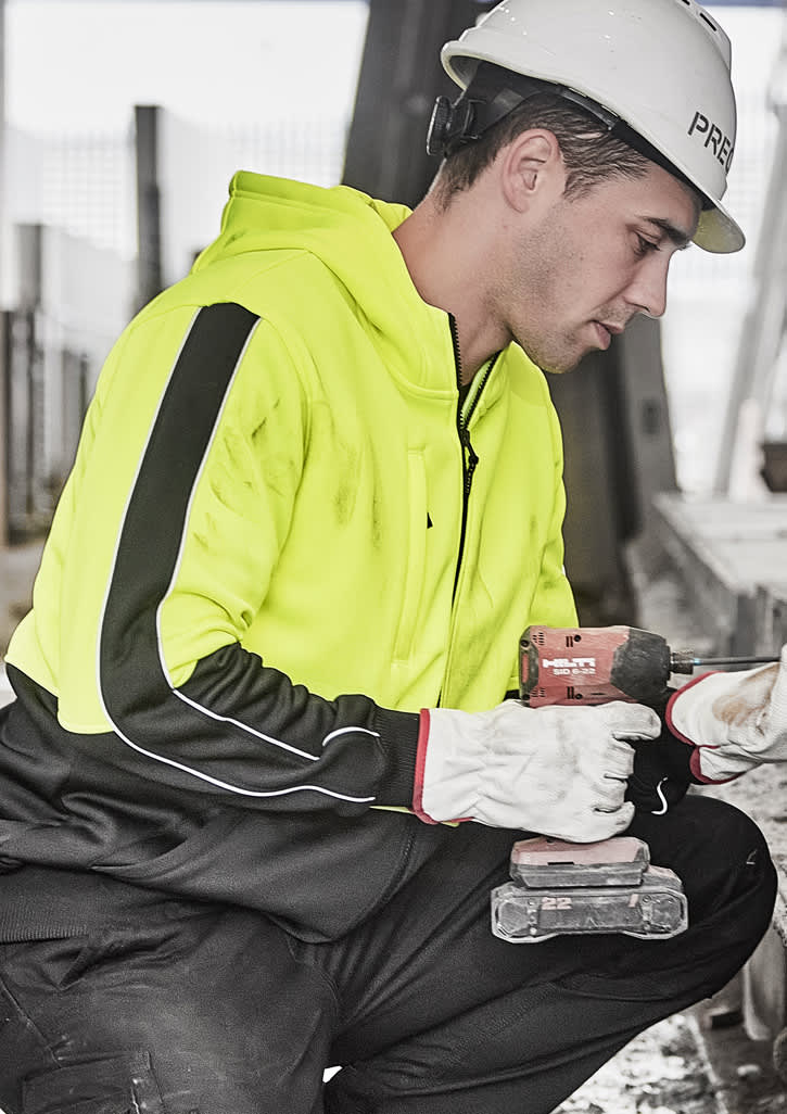 A unisex high visibility full zip hoodie in bright yellow with black accents, worn by a person holding a drill.