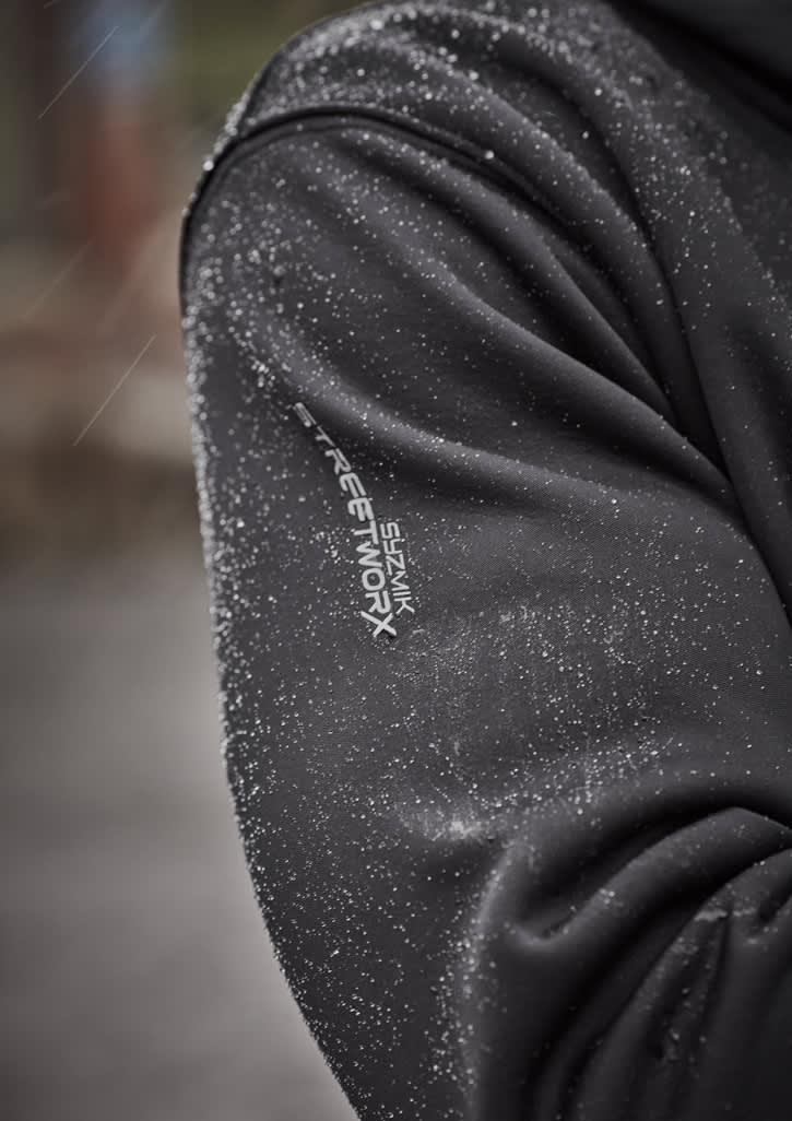 A unisex water-resistant hoodie in black, featuring a logo and pockets, worn by a model in a construction setting.