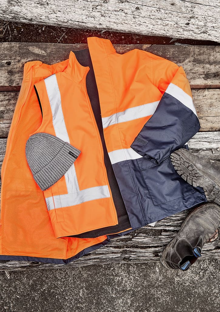 A reversible vest in orange and navy with reflective stripes, paired with a grey beanie and black work boots.