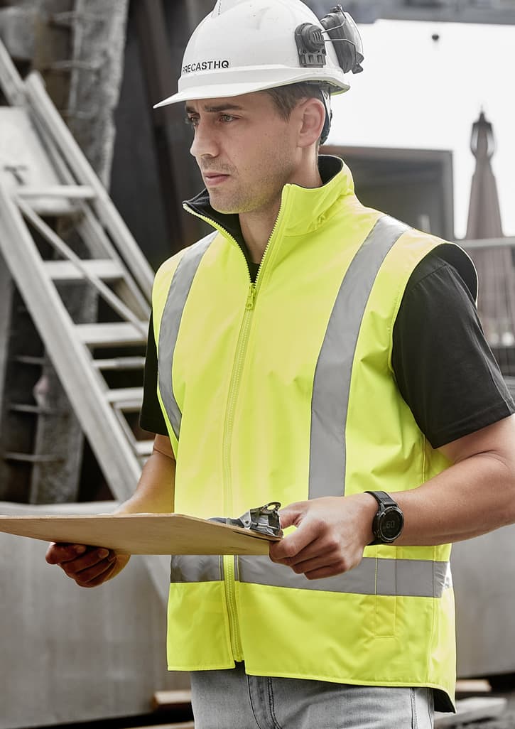A man wearing a bright yellow waterproof reversible vest with reflective stripes, holding a clipboard.