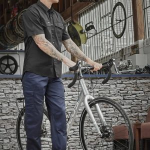 A man in a black shirt stands with a bike, wearing navy midweight drill cargo pants in a workshop setting.