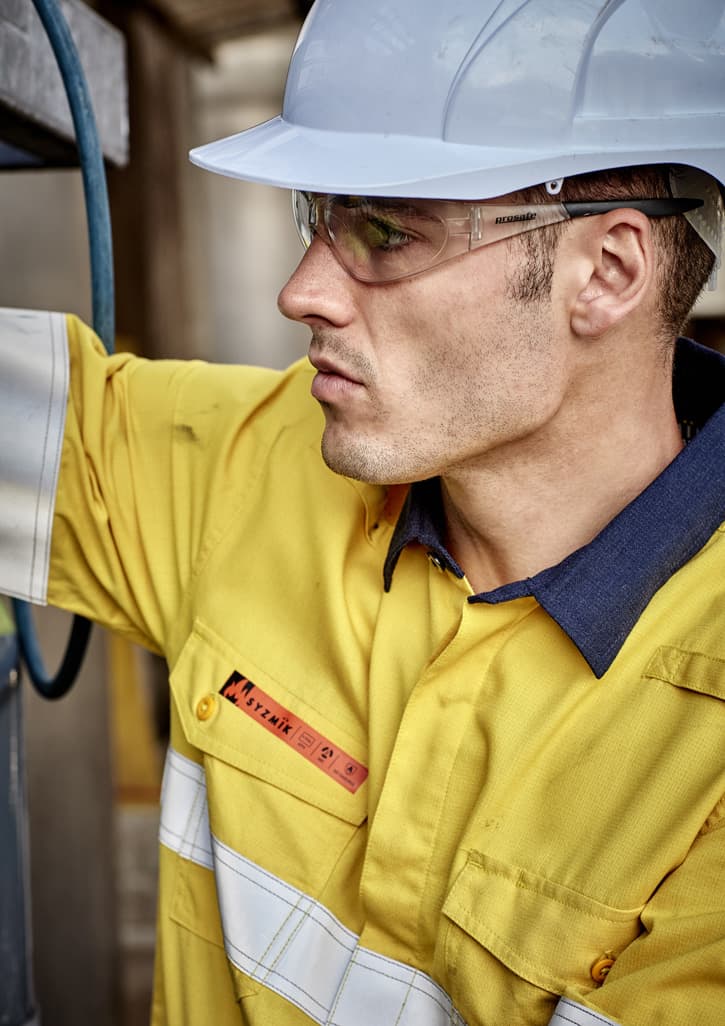A man wearing a yellow work shirt with white reflective strips and a blue collar, accompanied by safety glasses and a hard hat.