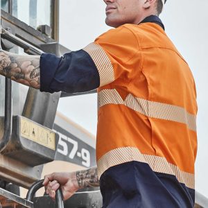 A man in an orange and navy long sleeve hi-vis shirt with segmented tape climbs a machine, wearing a white hard hat.