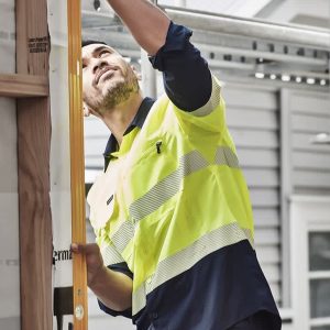 A man wearing a high visibility segmented tape long sleeve shirt in yellow and navy, working on a construction site.