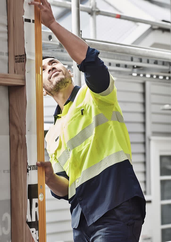 A man wearing a high visibility segmented tape long sleeve shirt in yellow and navy, working on a construction site.