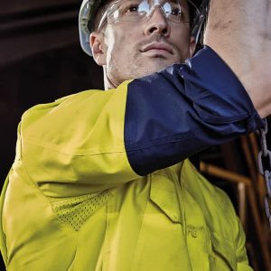 A men’s closed front long sleeve shirt in yellow and navy, featuring a logo, worn with safety goggles and a hard hat.