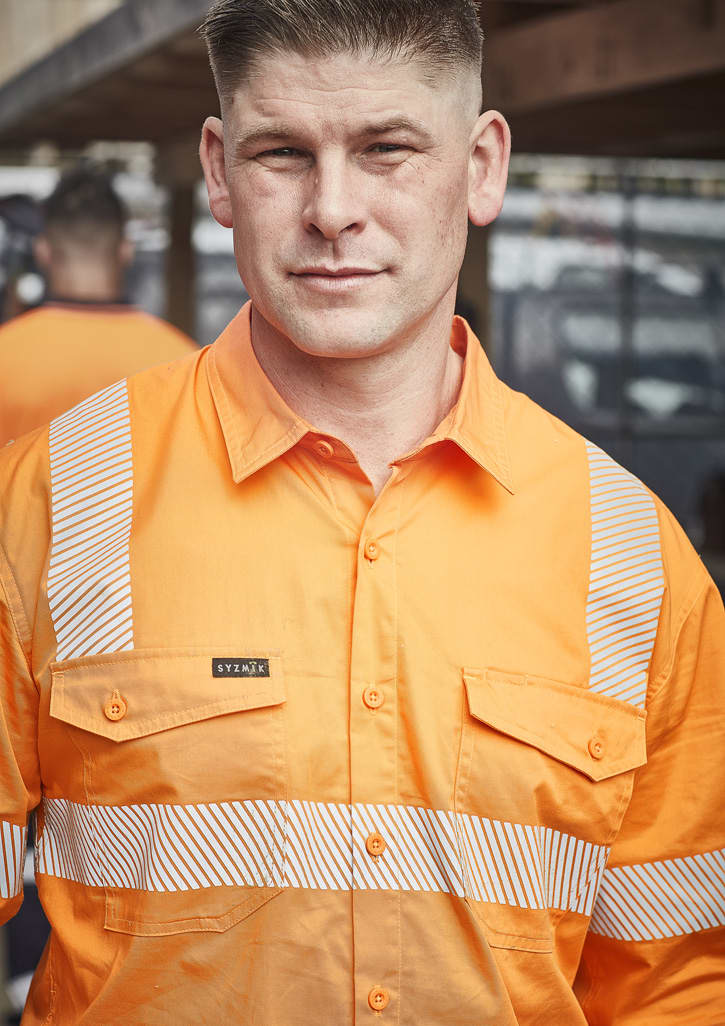 A man wearing an orange work shirt with segmented reflective tape and a logo on the front.