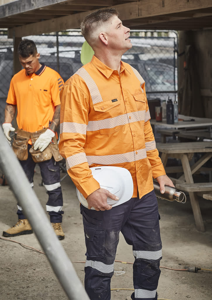 A bright orange men's work shirt with segmented tape, paired with navy pants, worn by a worker on site.