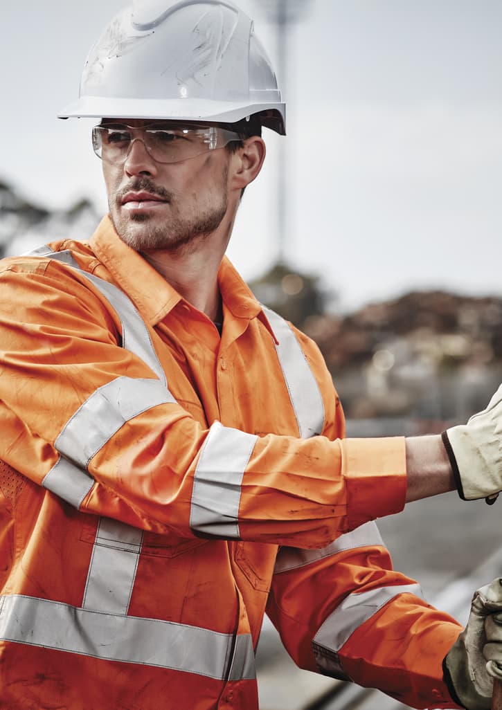 Hi-vis orange long sleeve work shirt with reflective tape, worn by a male worker in a construction setting, wearing safety gear.