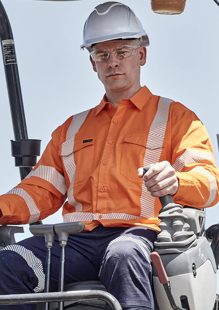 A man wearing an orange hi-vis shirt with segmented reflective tape operates machinery while wearing a white hard hat and safety glasses.