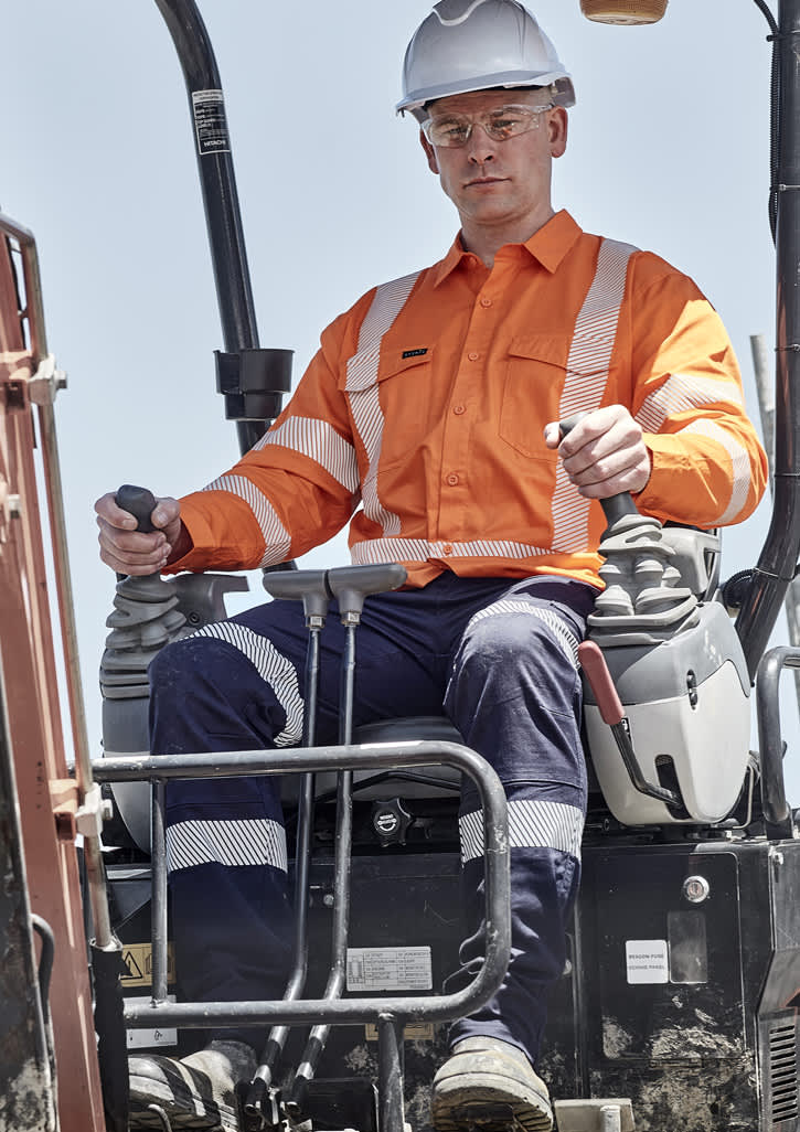 A man operates machinery wearing an orange Hi Vis shirt with segmented tape, alongside navy pants and a white hard hat.