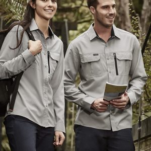 A man and woman wearing grey long sleeve button-up shirts with pockets, standing in a forested area.