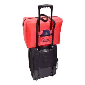 A red emergency travel bag is positioned on top of a black wheeled bag, with a passport visible in the front pocket.