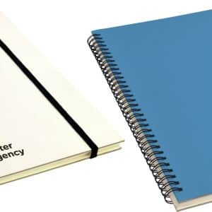 Two A4 notebooks with spiral binding, one white with a logo and one blue with a logo, featuring elastic closures.