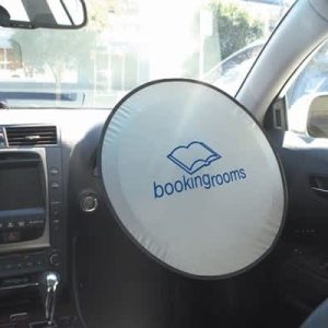 A circular sunshade for a car with a white exterior and a logo, placed on the steering wheel inside a vehicle.