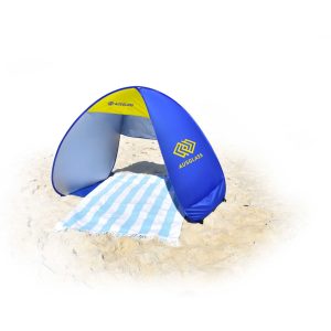 A blue and grey pop-up beach shelter with a striped towel on sand, featuring a logo on one side.