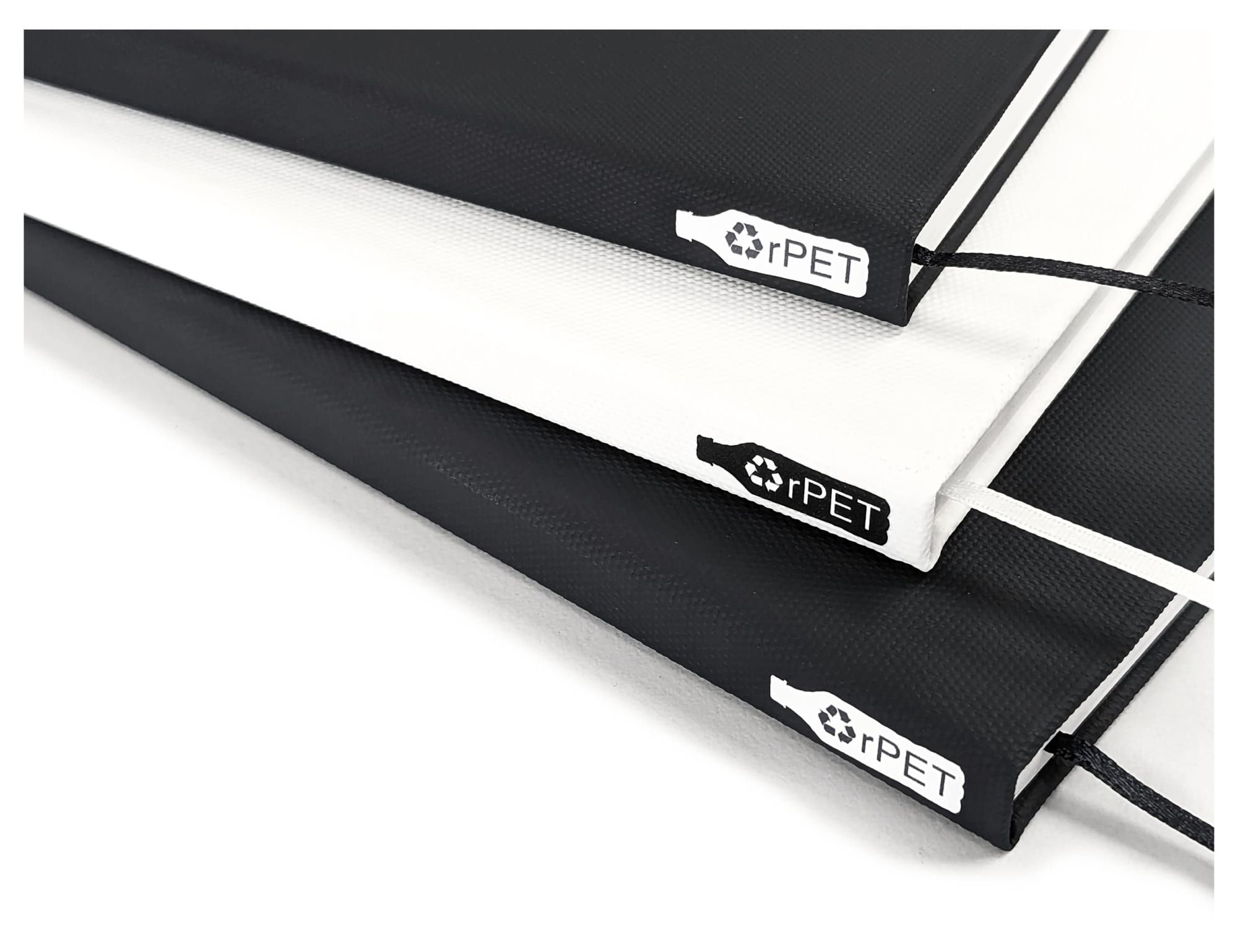 A series of A5 notebooks in black, white, and grey, featuring a logo and an elastic closure.