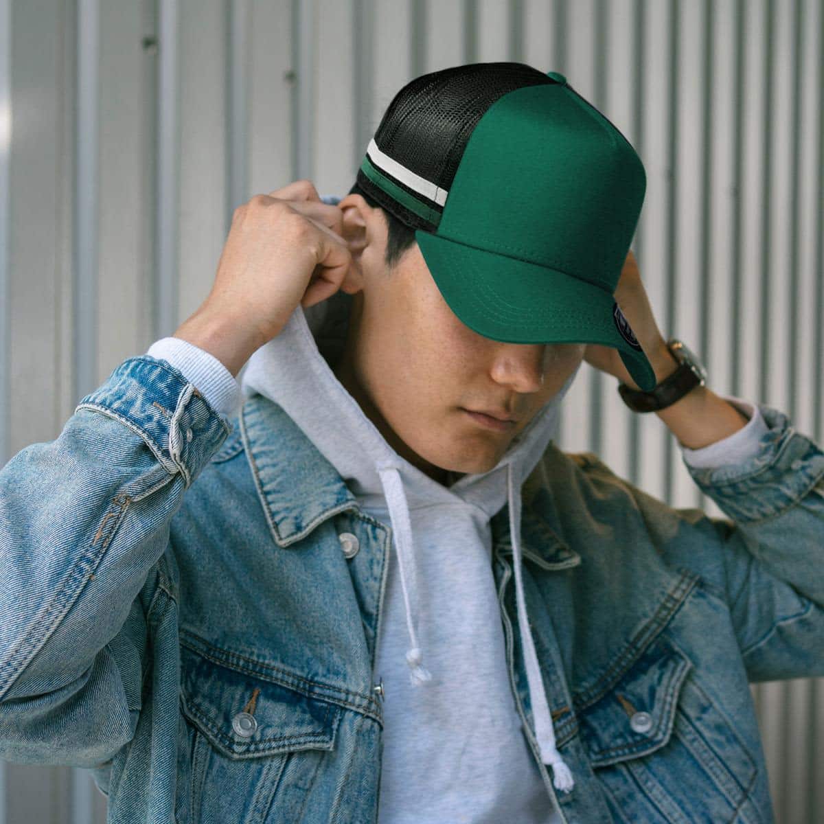 A green striped trucker cap with a black mesh back, worn by a person in a denim jacket and grey hoodie.