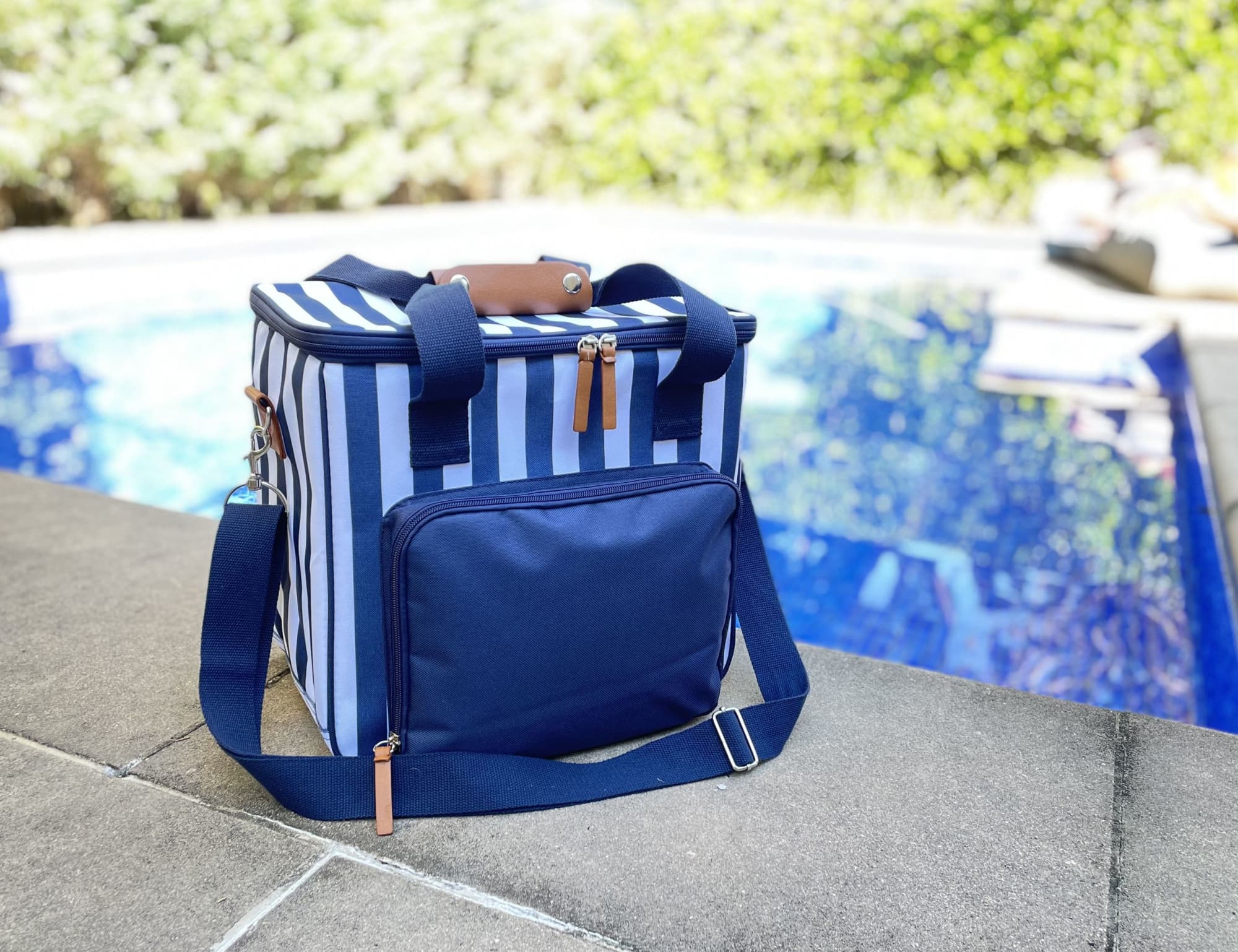 A navy cooler bag with blue and white stripes, featuring a shoulder strap and a front pocket. The bag has a logo.