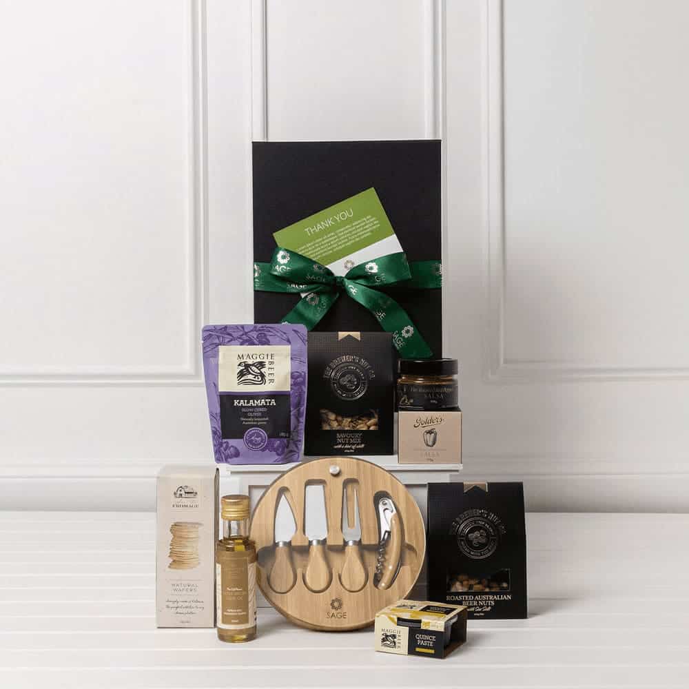 A gourmet gift pack featuring a wooden serving board, assorted gourmet snacks, olive oil, and a jar of jam, all in a black box.