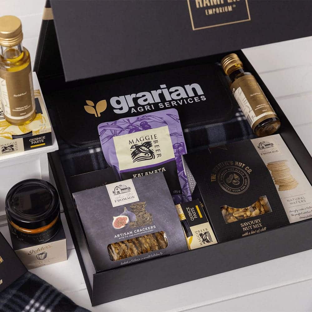 A gourmet picnic gift pack filled with olive oil, crackers, nuts, honey, and a branded box in black and white.